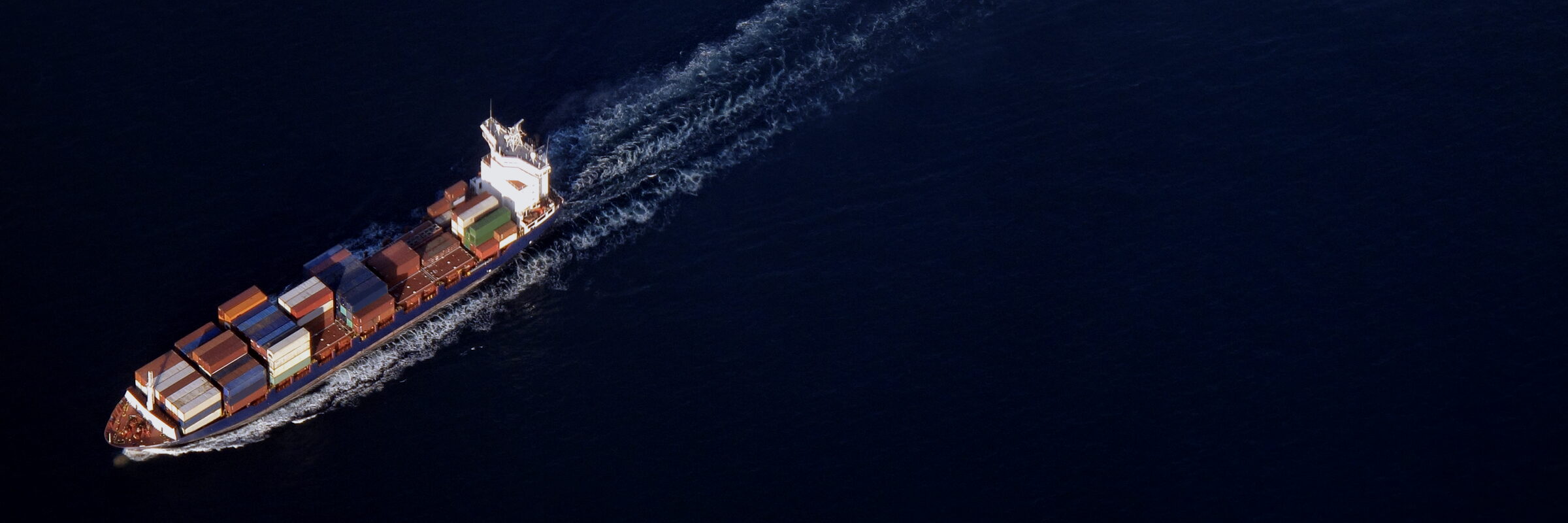 Container ship crossing open sea, seen from above, with a long wake