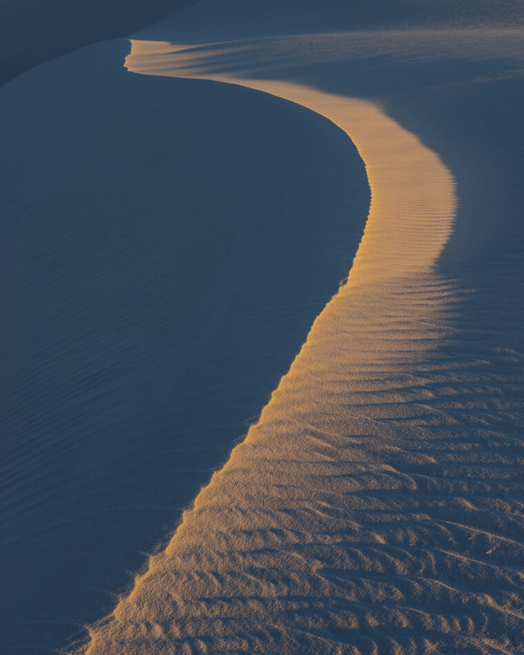 Aerial view of desert dunes with a golden lit ridge