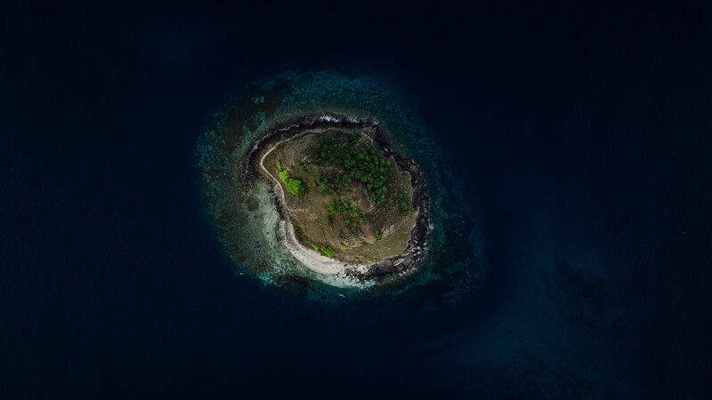 Small island surrounded by deep navy sea, seen from above